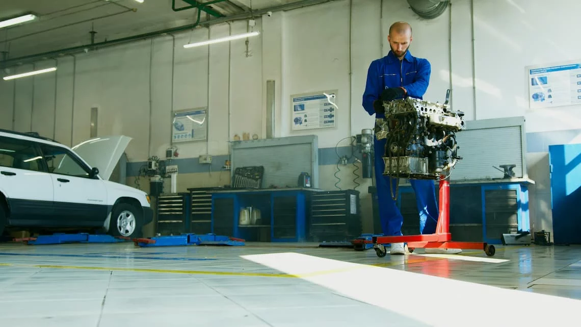 Auto repair mechanic working on a removed car engine in an independent shop bay, illustrating the kind of equipment lease payment processing trap that keeps merchants paying after their main contract ends