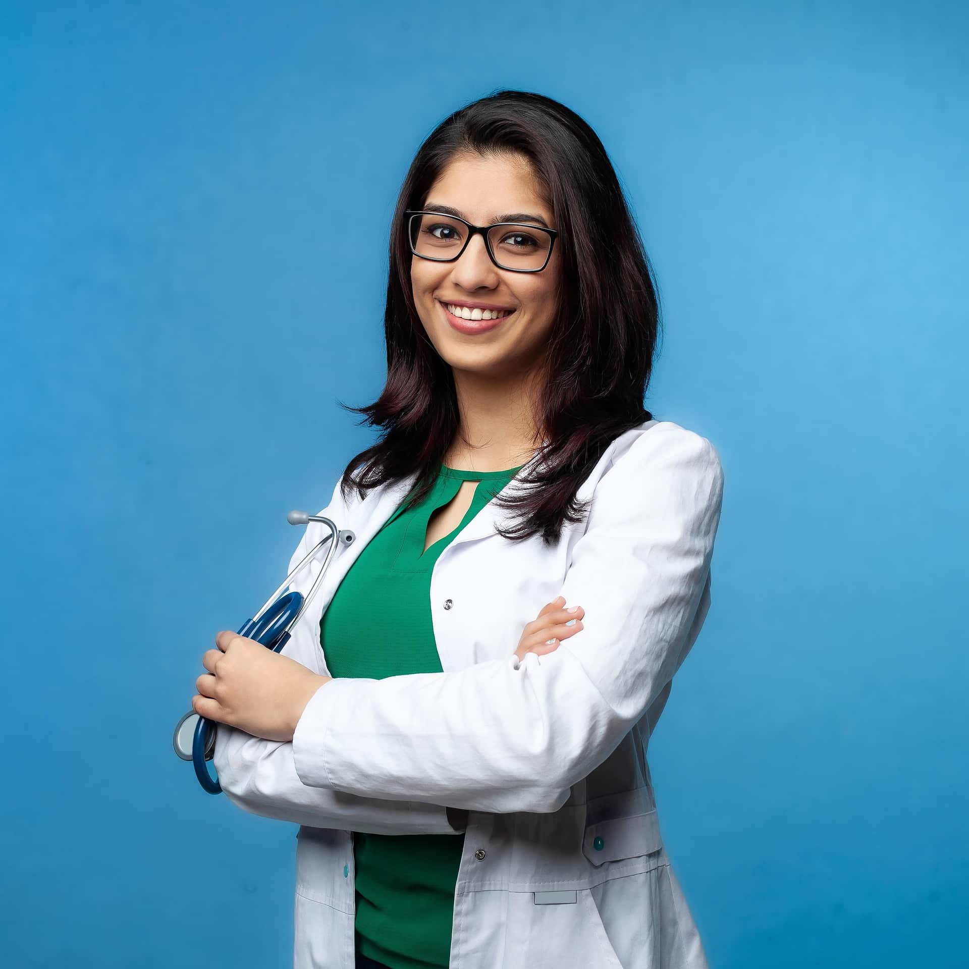 PCI non-compliance fee discovered by physician — young Indian-American internist in white coat with stethoscope, the kind of first-time solo-practice owner who discovers the monthly PCI non-compliance fee on her statement after her CPA flags it during tax prep