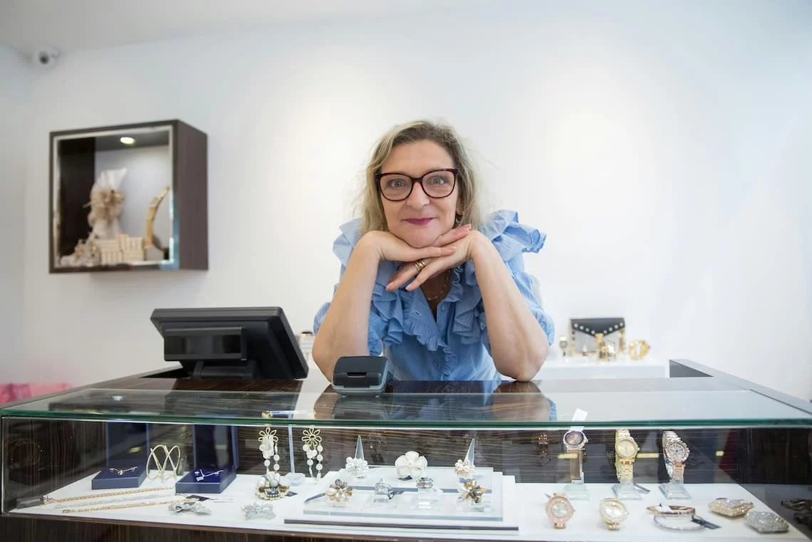 A Charleston jewelry boutique owner reviewing two payment processing scenarios on a tablet — accepting all credit cards versus declining premium cards under the new Visa-Mastercard 2026 settlement rules