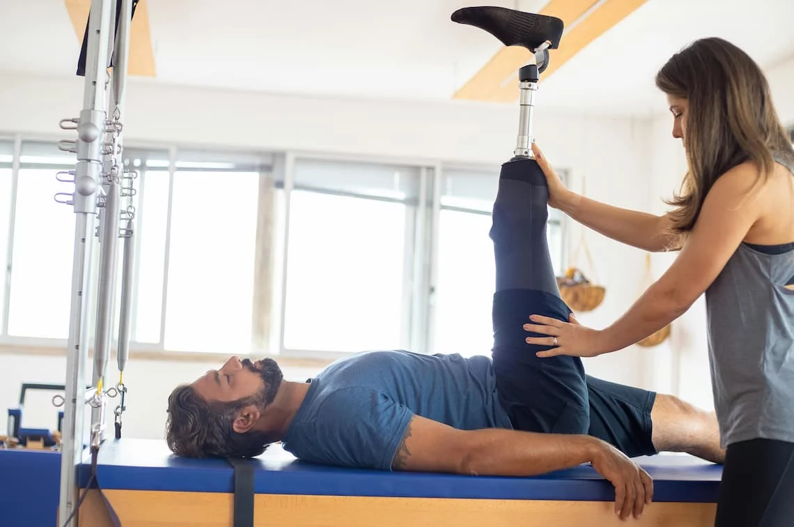 Physical therapy payment processing in practice — a therapist guiding a patient through a leg exercise on a reformer table in a bright clinic