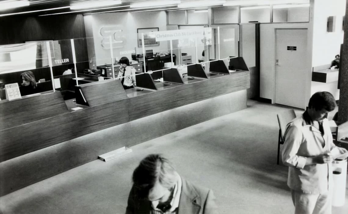 A black-and-white photo of a 1980s bank teller counter - the kind of dated payment infrastructure behind many government payment processor complaints