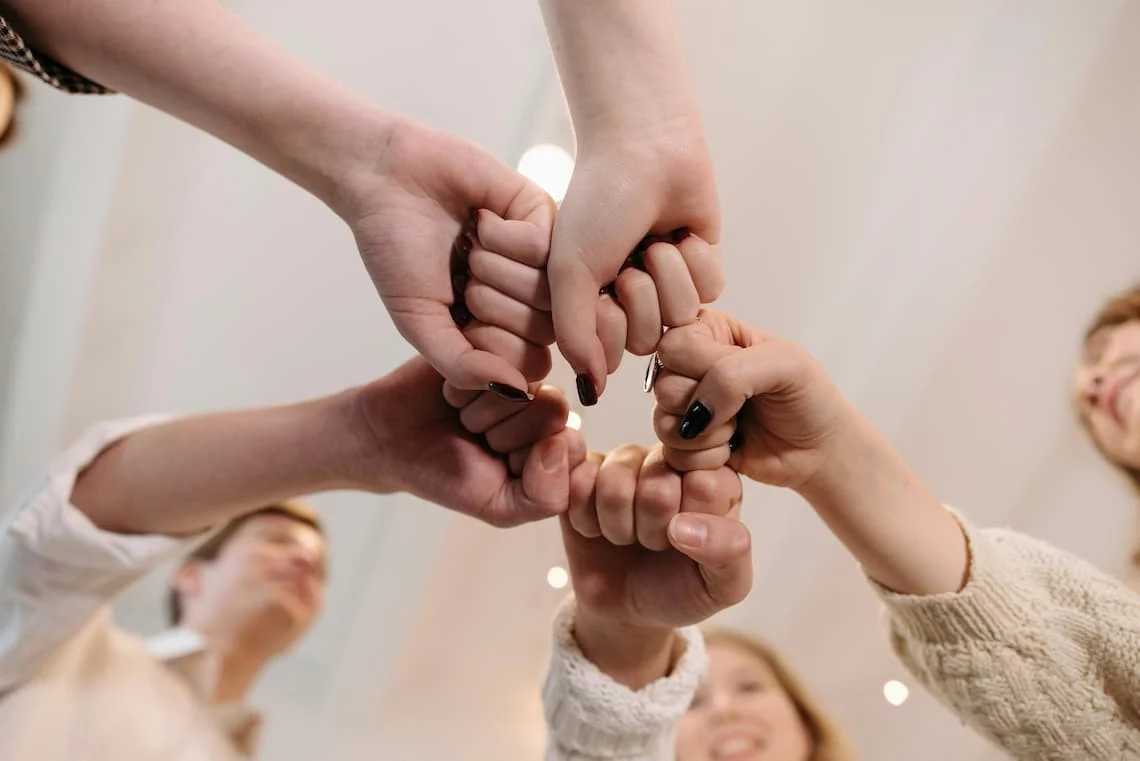 several hands stacked together on grass representing membership pricing payment processing as a shared wholesale buying club