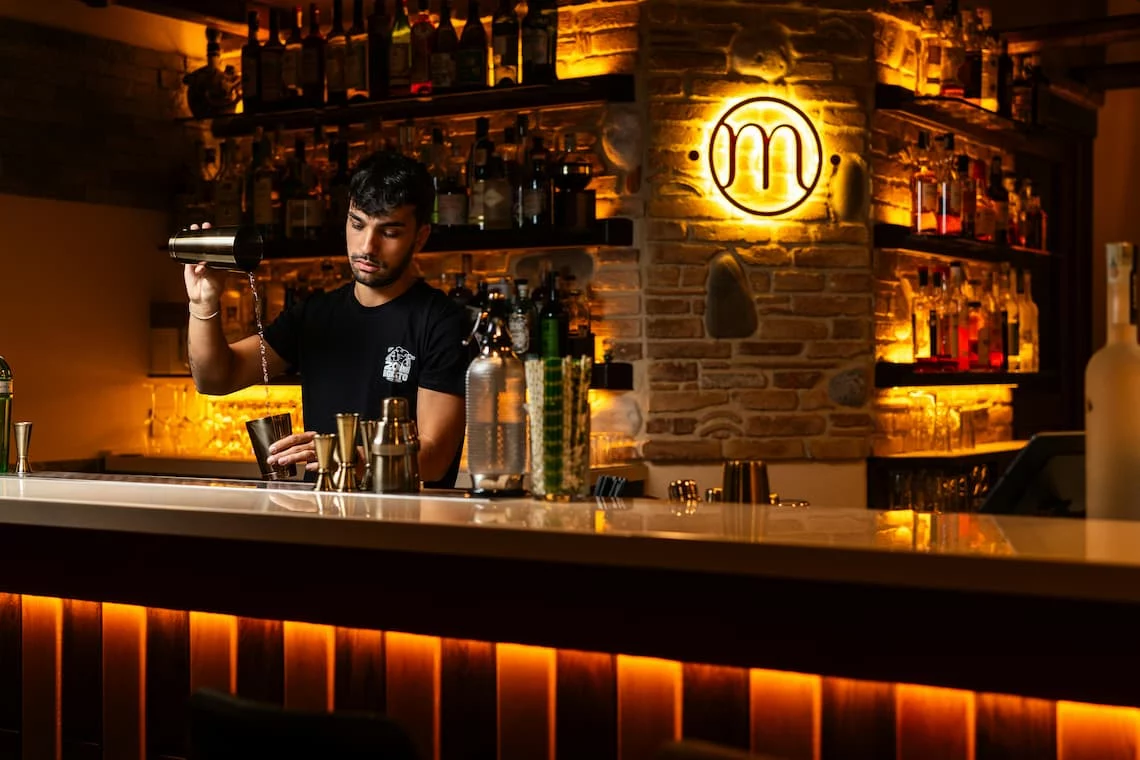 Bartender mixing a cocktail behind a warm neighborhood bar — bar payment processing fees