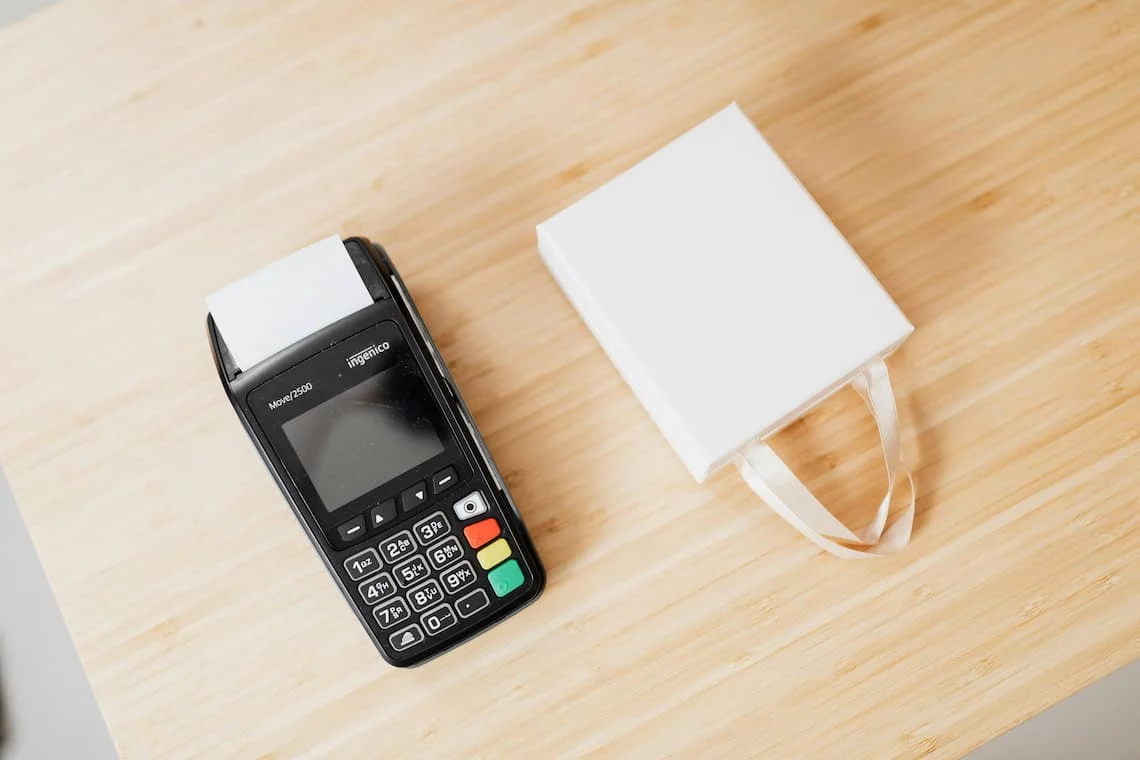 A free credit card terminal beside a white gift bag on a wood counter